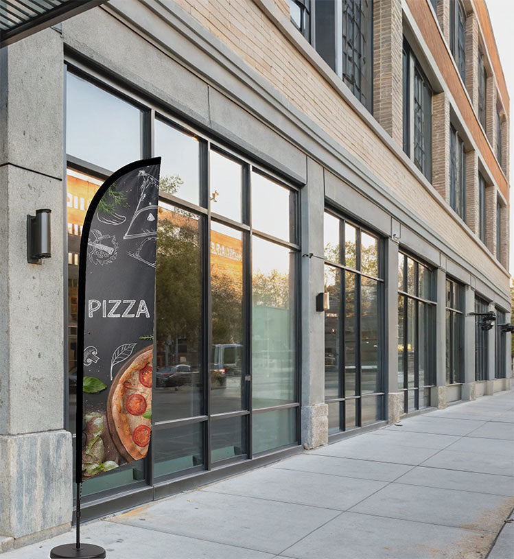 Feather flag “Pizza” noir style ardoise avec illustrations blanches, installé devant une pizzeria moderne